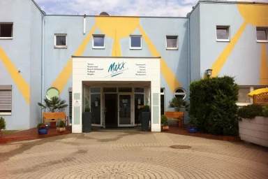 Eingang zu einem modernen Gebäude mit orangefarbenen Akzenten und Pflanzen auf dem Gelände.